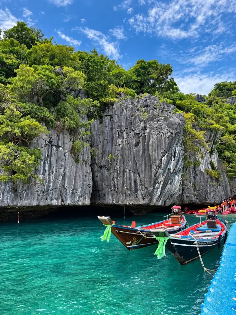 Boats and kayaks by a limestone cliff in Ang Thong