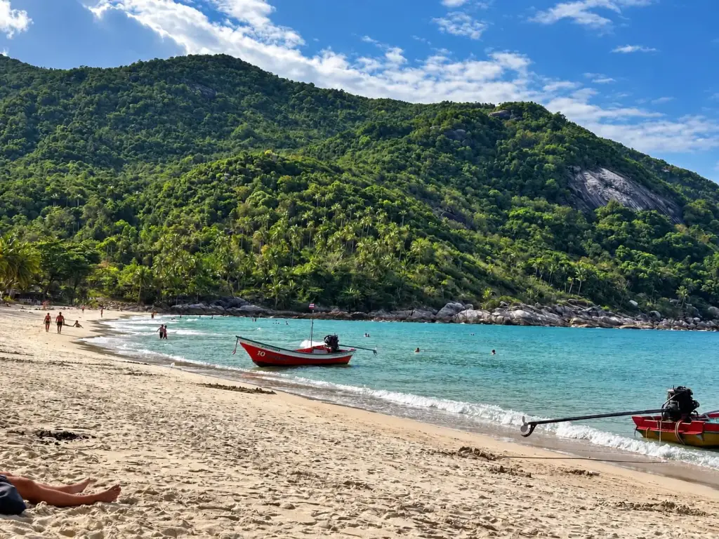 Longtail boats in the bay at Bottle Beach, with the green mountain behind