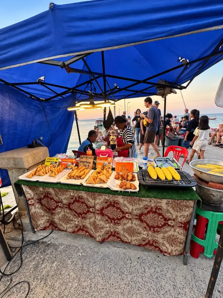 Food stall at the Chaloklum Sunday market, with the sea behind