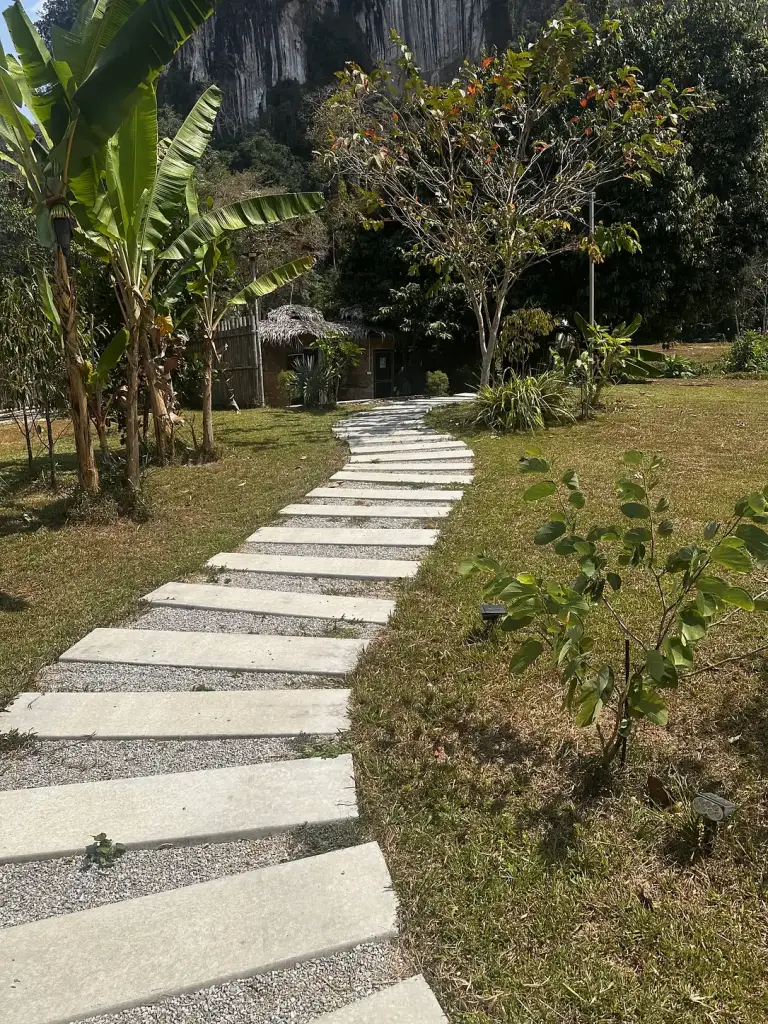 A stone path between banana trees, with limestone cliffs above Cosy Garden