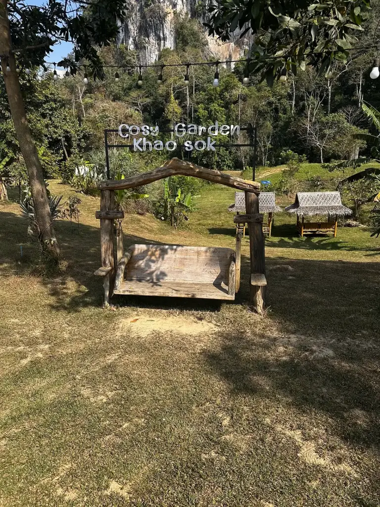 A wooden swing and the Cosy Garden Khao Sok sign, with limestone cliffs behind