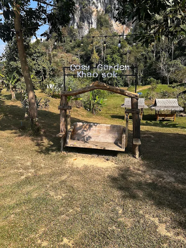 Wooden swing and Cosy Garden Khao Sok sign, with limestone cliffs behind