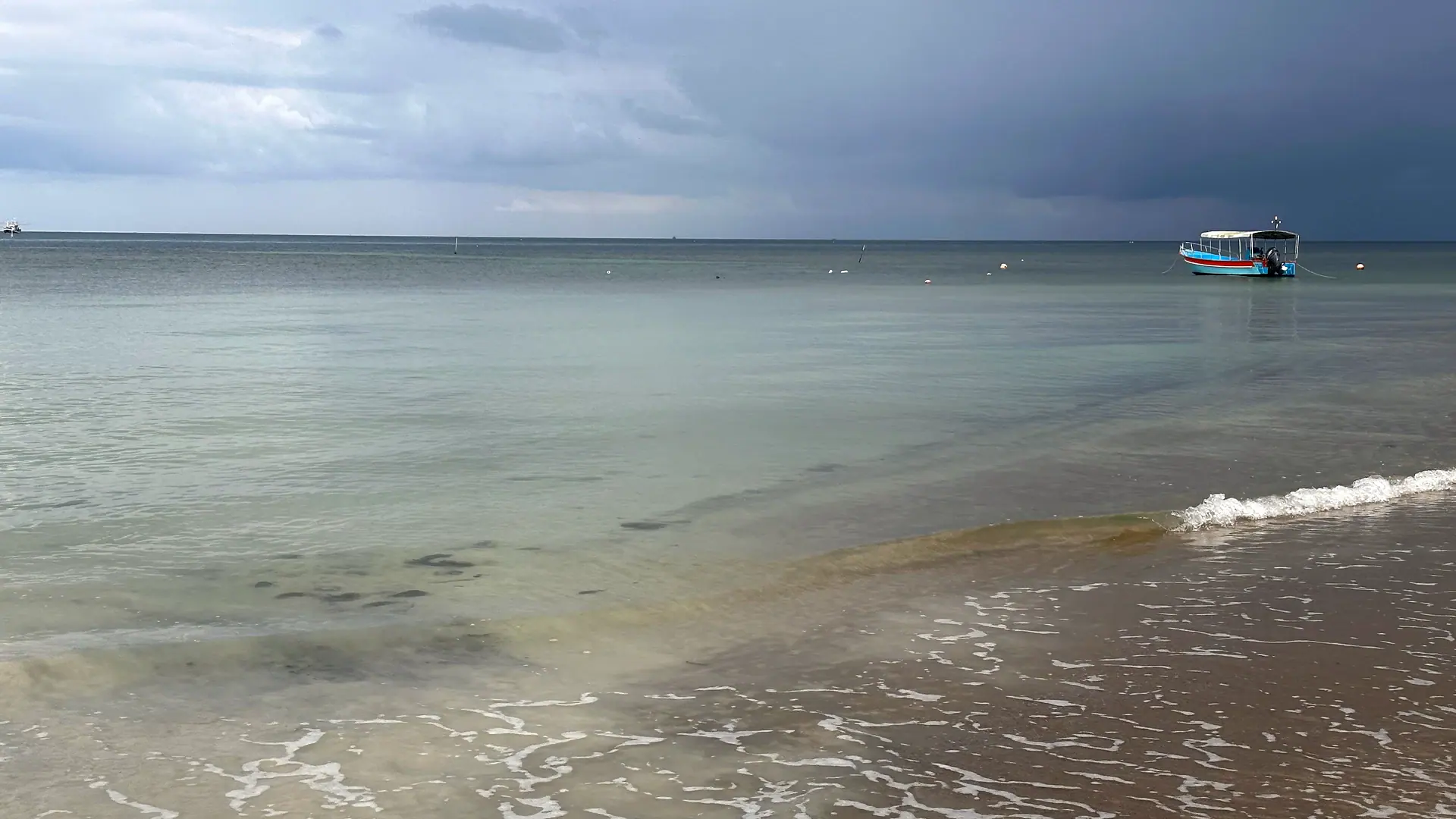 Der Strand von Haad Yao an einem stürmischen Morgen: klares Wasser, eine kleine Welle und ein Boot in der Bucht, Koh Phangan