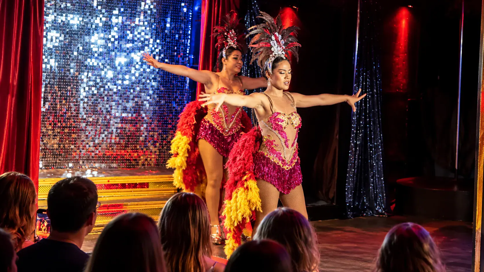 Two performers in pink feathered costumes in front of the sequin wall on stage at Queen's Cabaret, Koh Tao