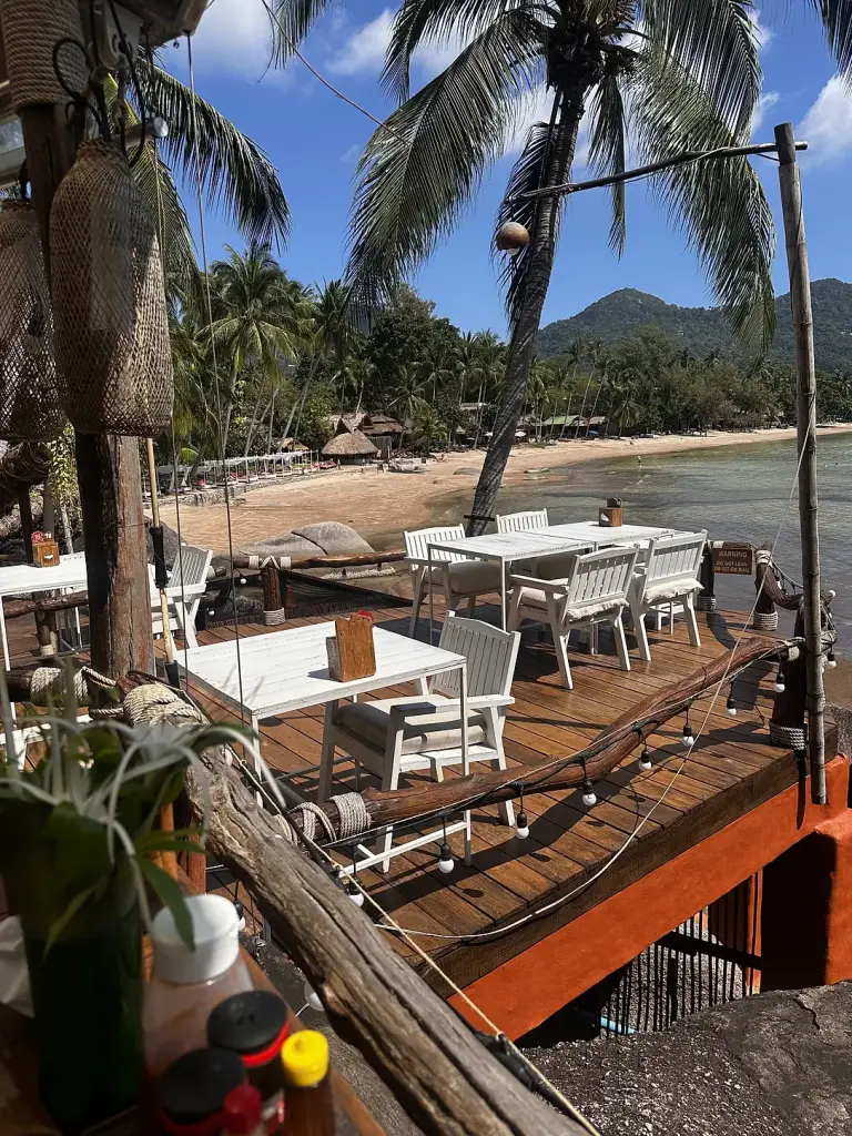 Witte tafels op een houten terras boven de rotsen bij Rim Lae, met uitzicht op Sairee Beach