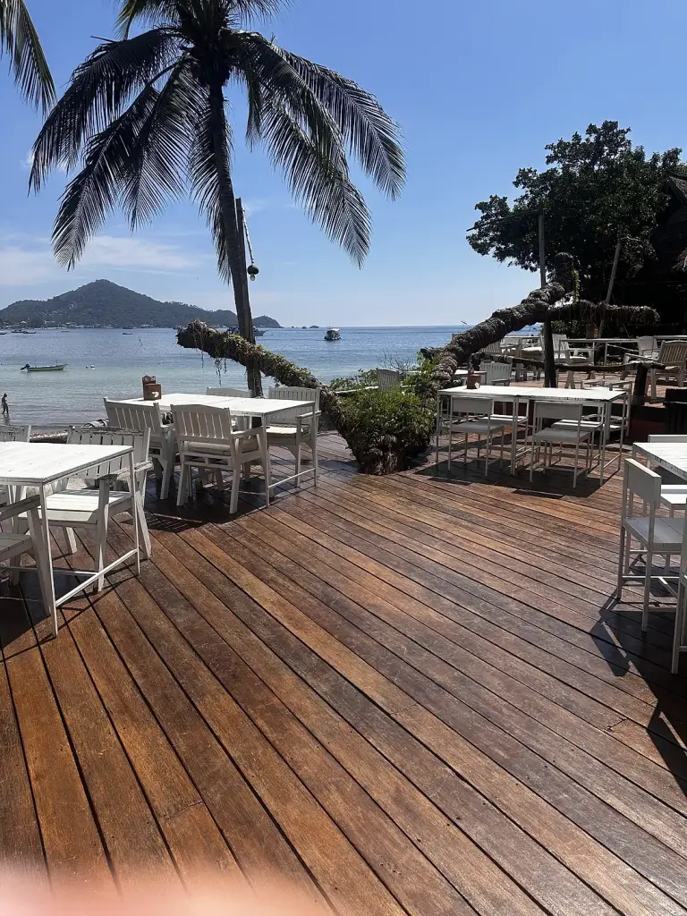 Houten terras met witte tafels en palmen met uitzicht op zee bij Rim Lae, Koh Tao