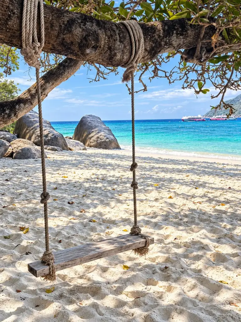 A rope swing on a white beach between granite boulders, Similan Islands