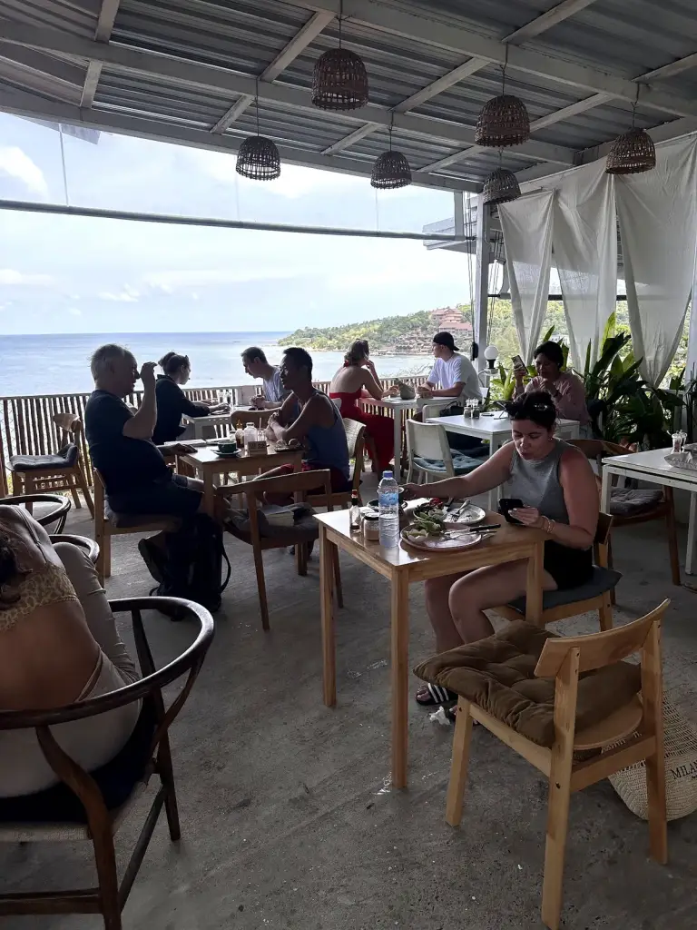 La terrasse couverte de What's Cup, avec ses tables en bois, ses abat-jour tressés et sa vue sur la baie